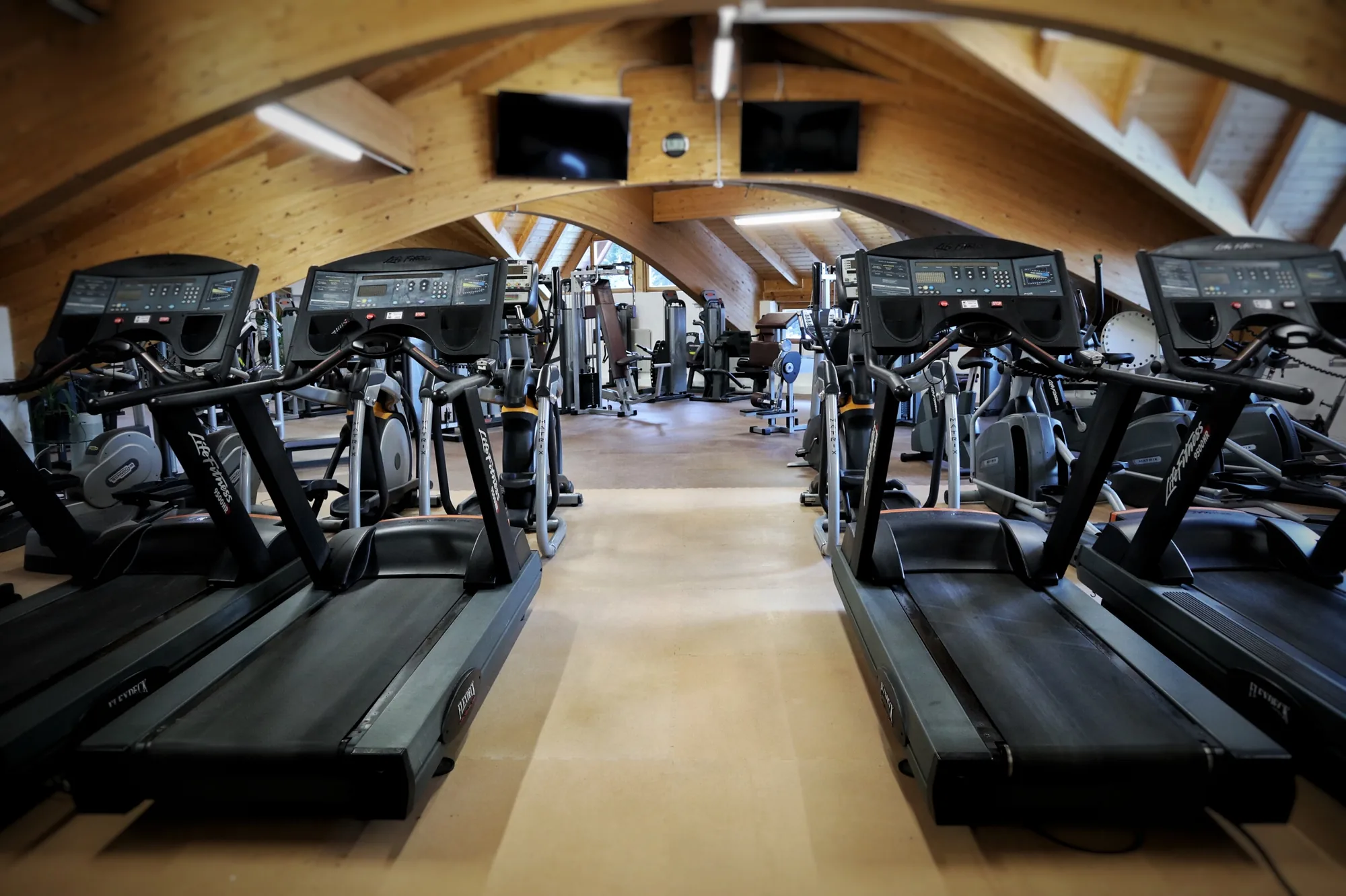 Zona cardio con tapis roulant Life Fitness ed ellittiche sotto le travi in legno ad arco